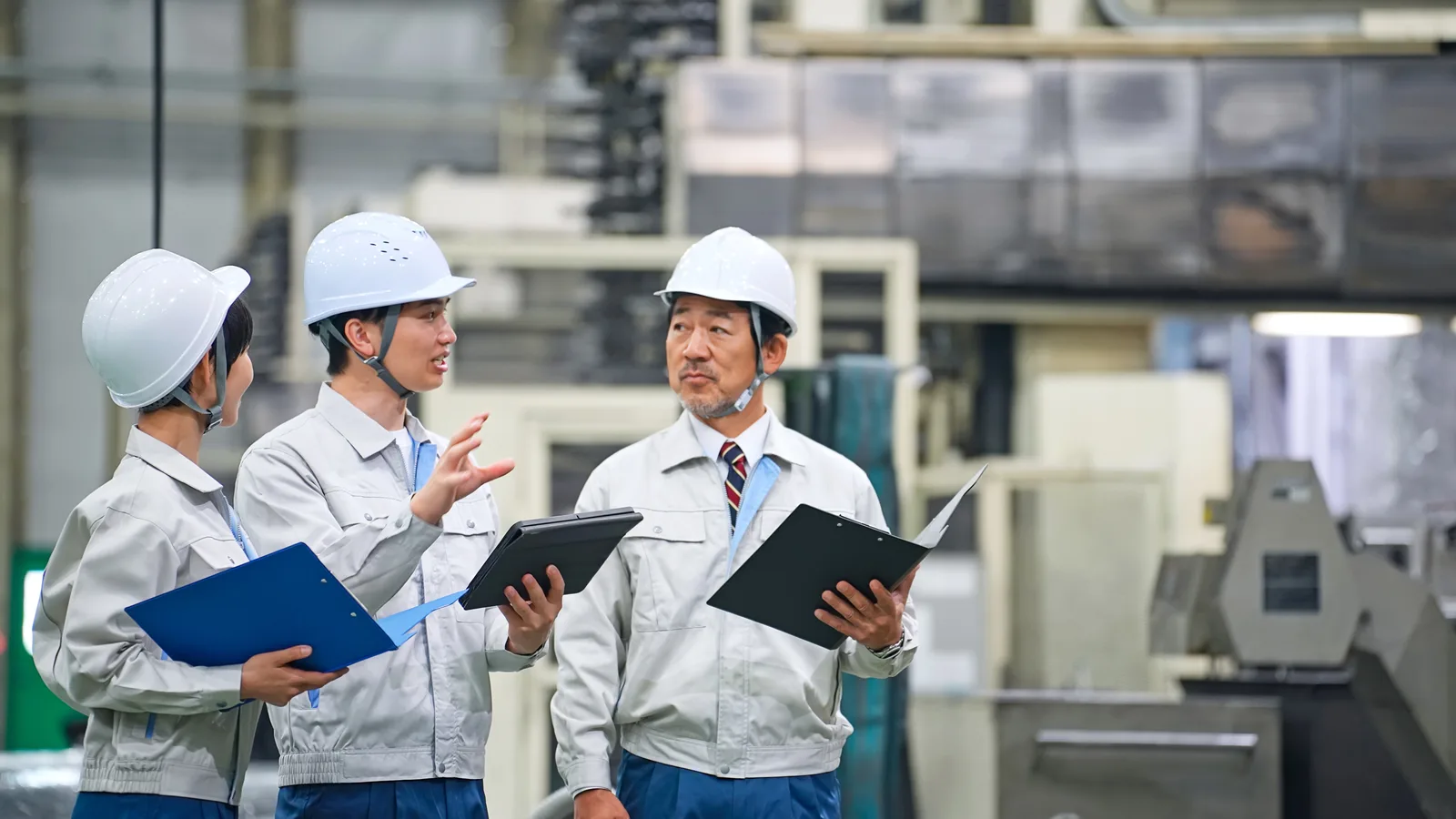 工場で書類を見ながら話す作業着の社員